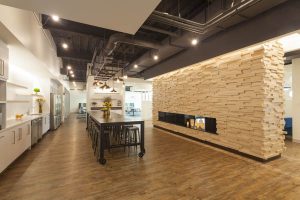 The main cafeteria area features a welcoming faux fireplace wall, an industrial oiled steel bar and restaurant-style seating areas.     