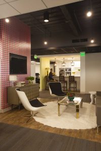 This collaboration zone highlights a contemporary living area, which features products available on the Wayfair.com website. Modern seating, a shag rug and pink houndstooth wallcovering warm up the office environment.